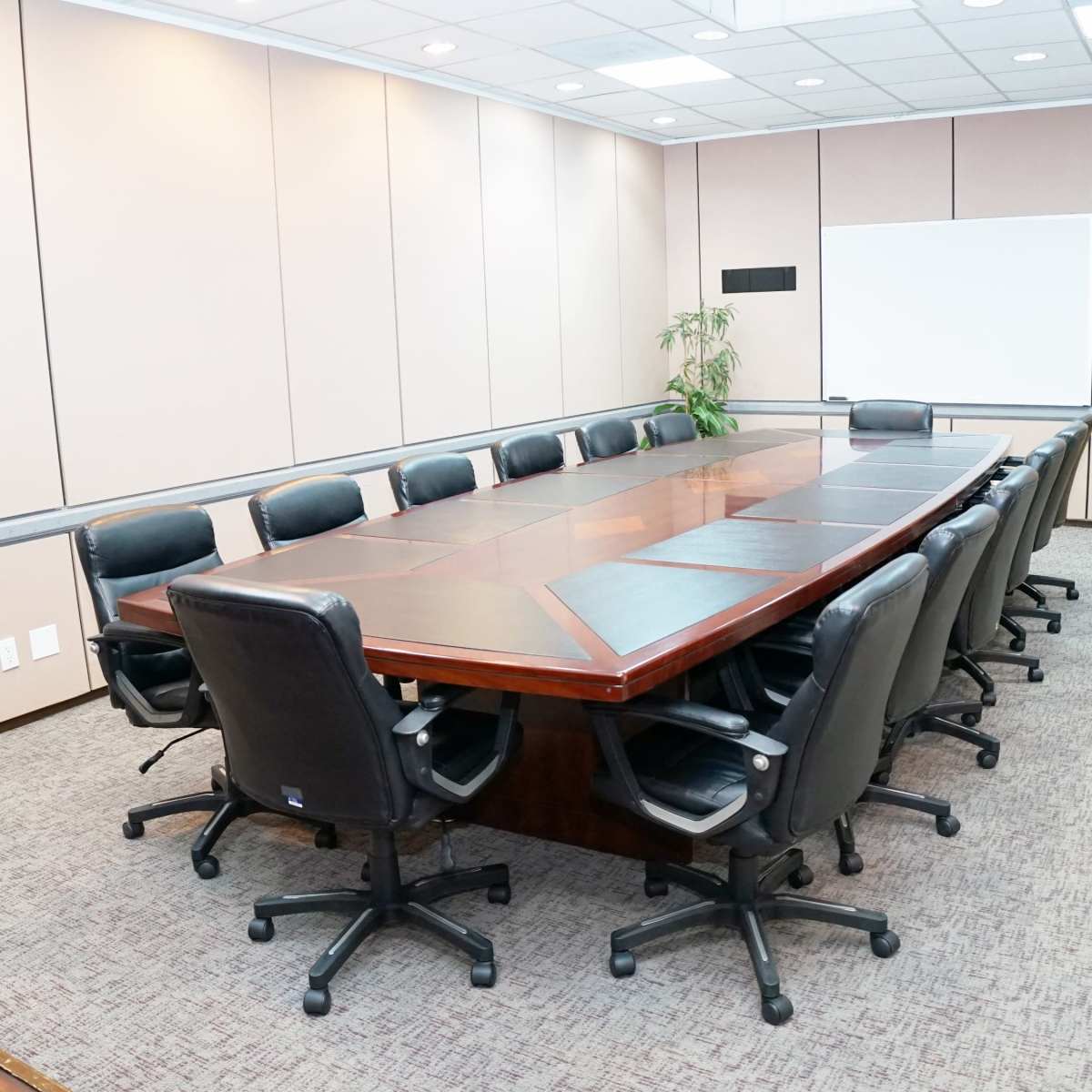 A long wooden conference table surrounded by black rolling chairs is set in a well-lit meeting room.