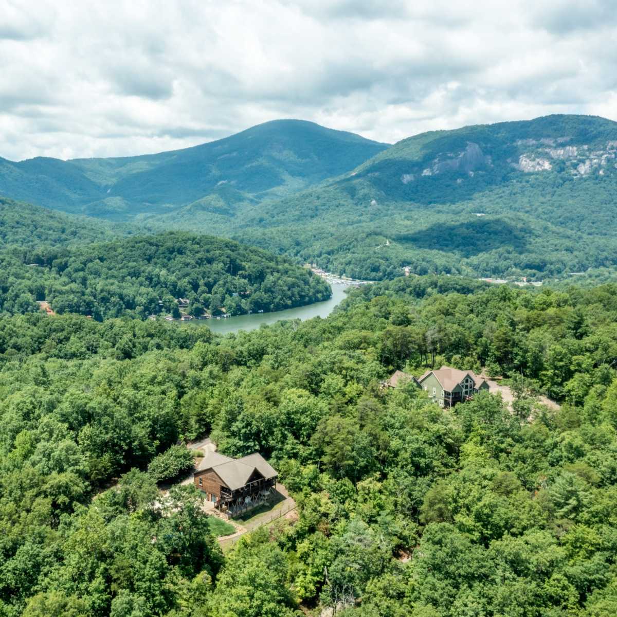 A scenic view of a lush green landscape with mountains in the background, a river winding through the valley, and a few houses nestled among the trees.
