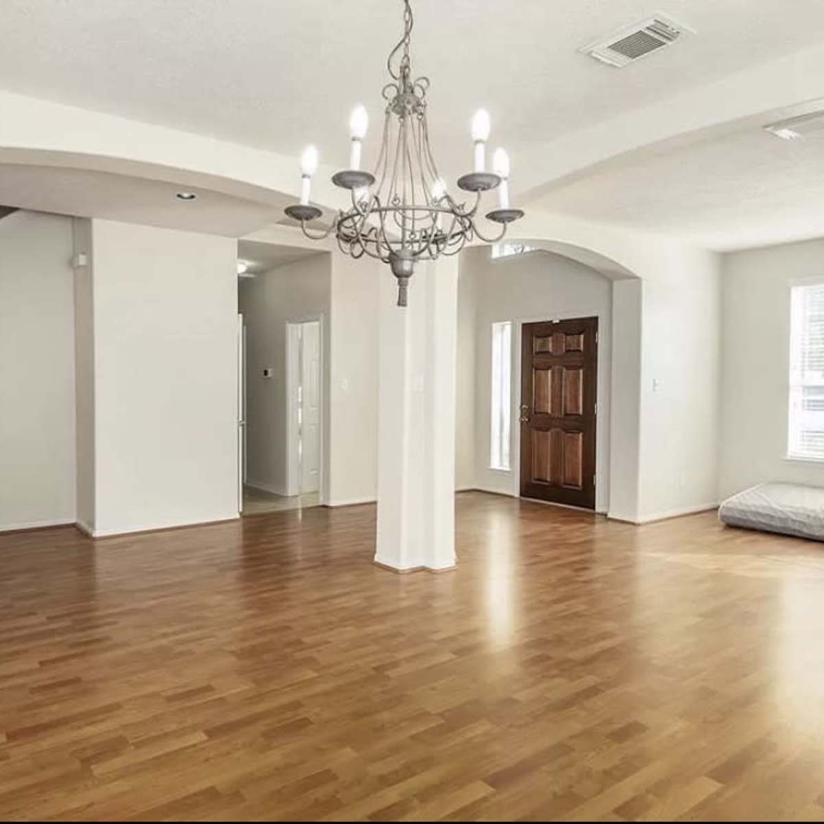 The spacious interior features wooden flooring, arched doorways, and a chandelier hanging from the ceiling.