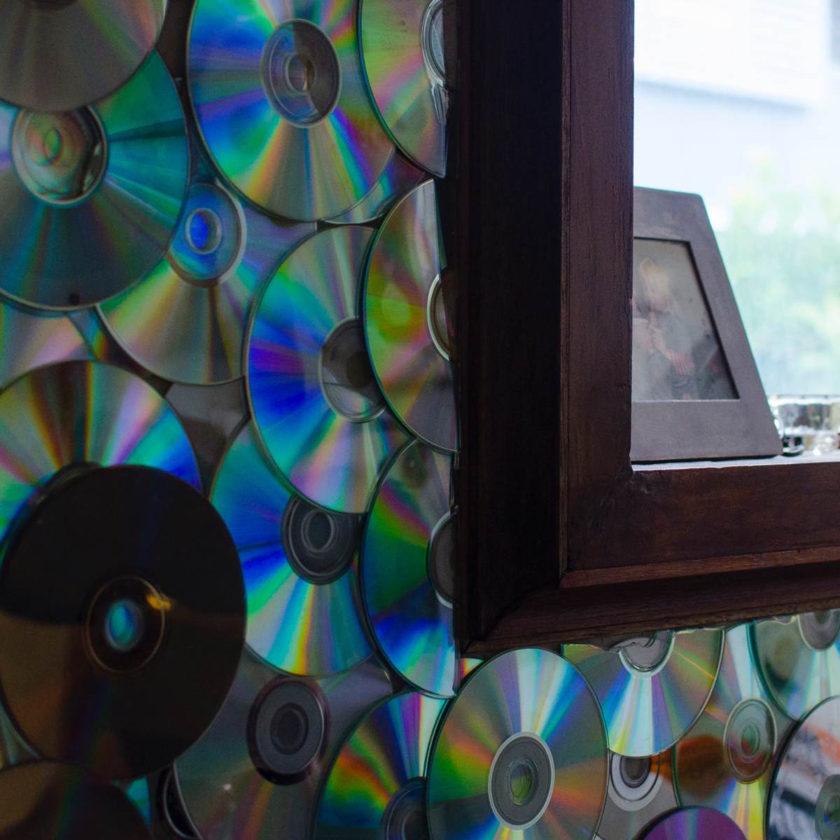 A wall covered with shiny, colorful CDs and a wooden window frame displaying decorative items.