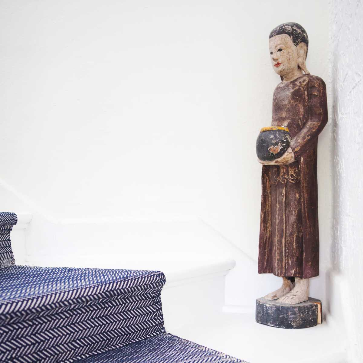 A wooden statue stands next to a white staircase covered with a patterned runner.