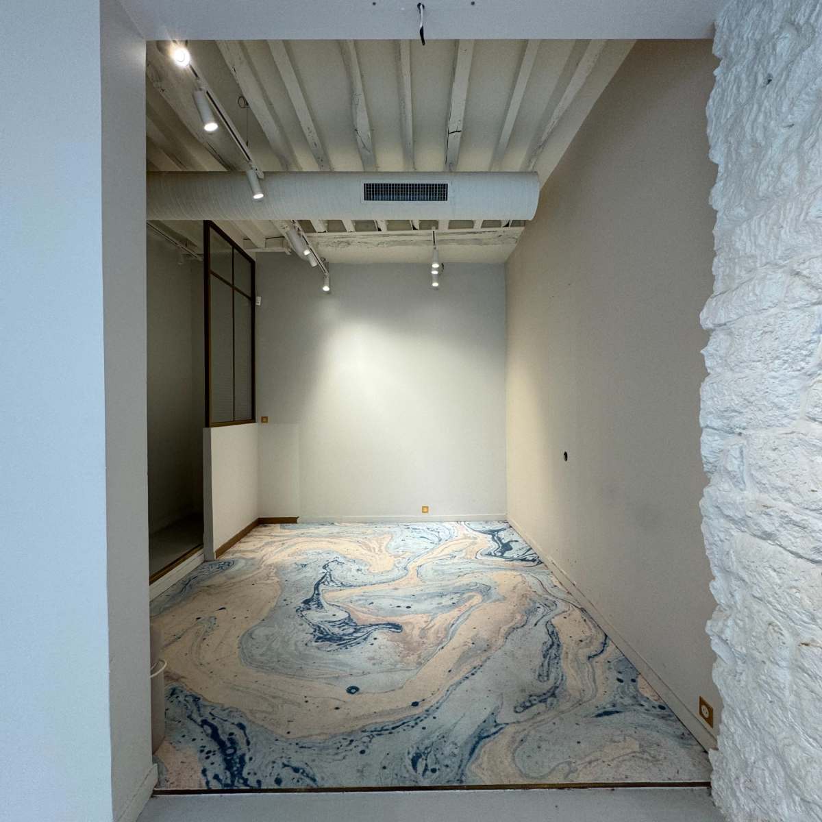 An empty room with a marbled blue and beige carpet and a textured stone wall on one side.