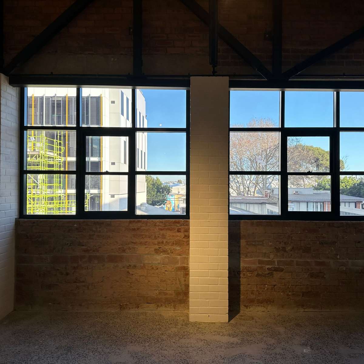 A room with brick walls and large windows, offering a view of the outside buildings and clear skies.