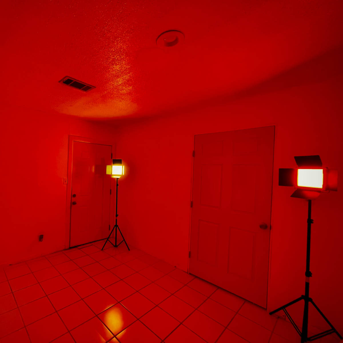 A small room illuminated by red lights, featuring a door on one wall and a second door on an adjacent wall.