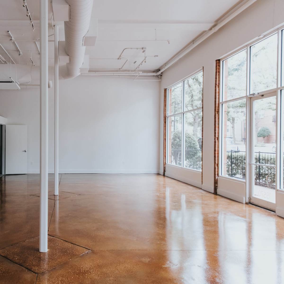 A spacious, empty room with polished concrete floors and large windows letting in natural light.