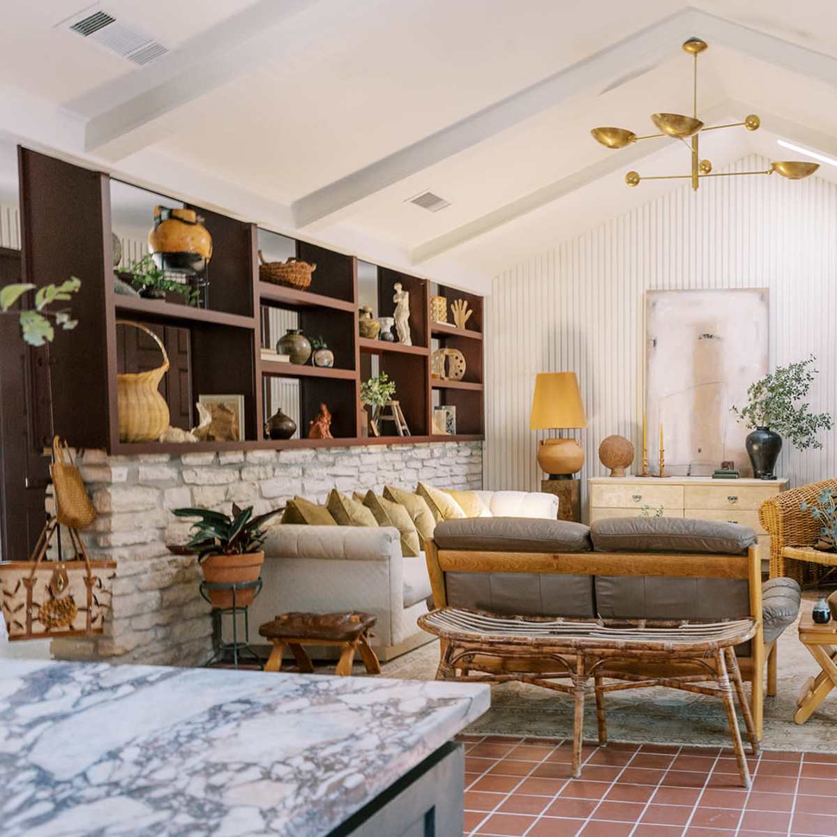 A well-decorated living room with a stone fireplace, a mix of furniture styles, and shelves adorned with decorative items.