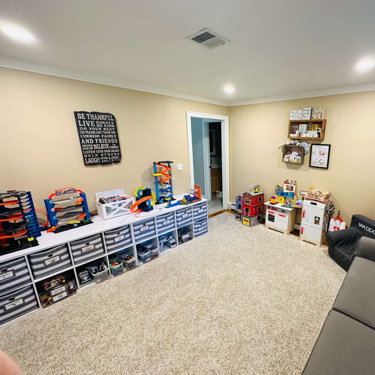 A playroom features organized storage containers filled with toys, a sofa, and wall-mounted shelves displaying various items.