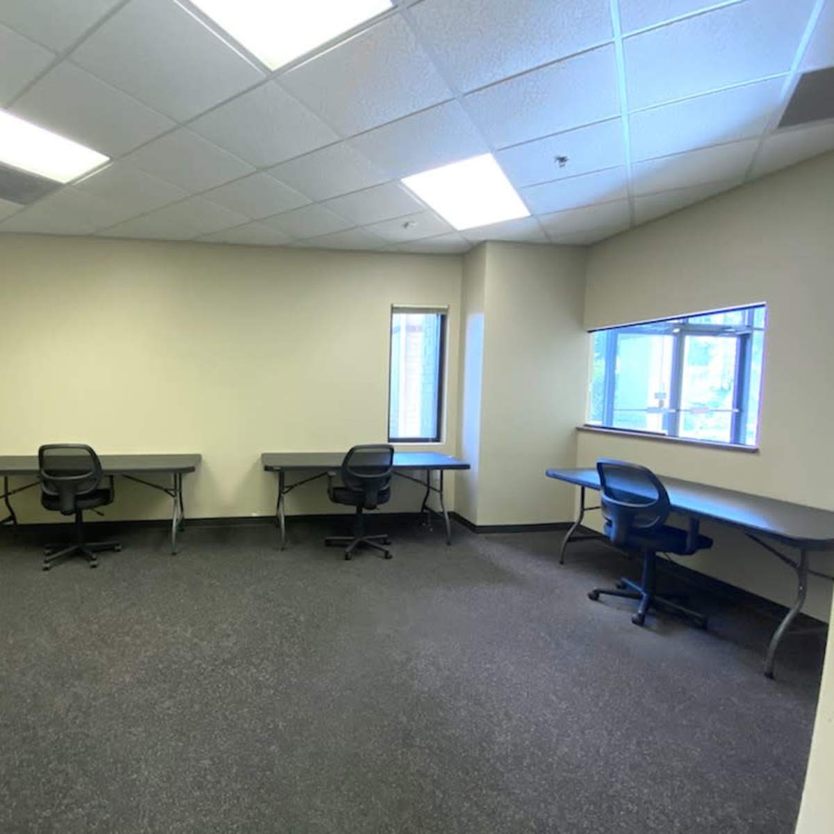 An empty office space with three tables and chairs arranged along the walls.