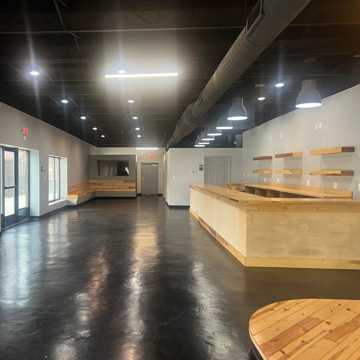 A spacious interior with polished black floors, wooden counters, and ample natural light coming through large windows.