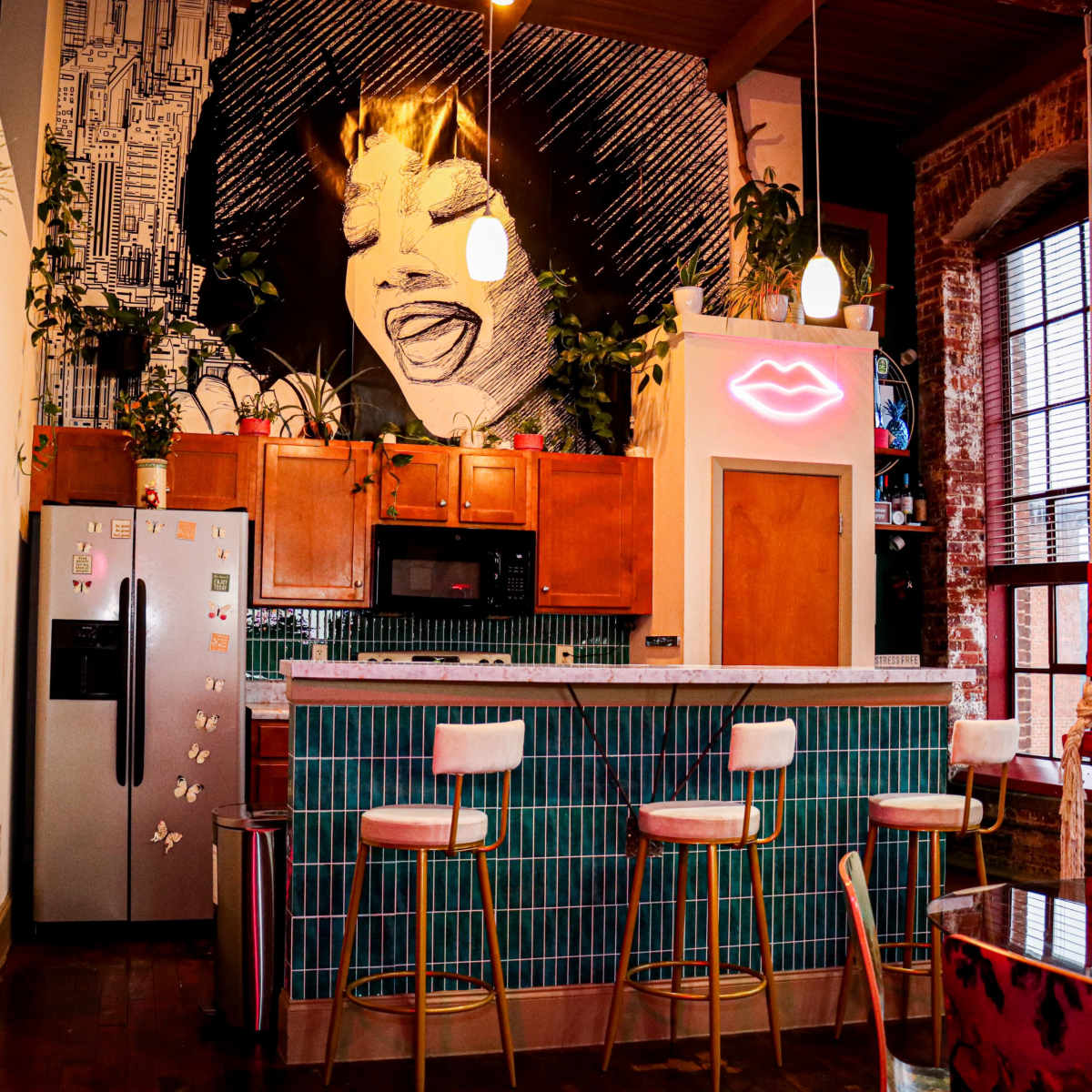 A stylish kitchen with a large mural of a smiling woman, accompanied by bar stools and vibrant tile accents.
