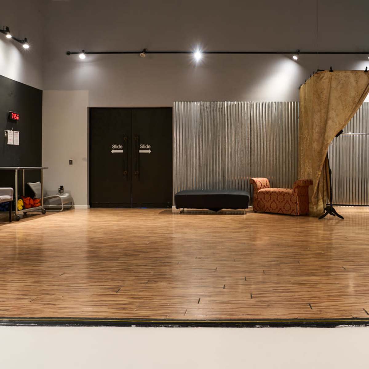A spacious studio with wooden flooring, featuring a seating area and a backdrop with curtains.