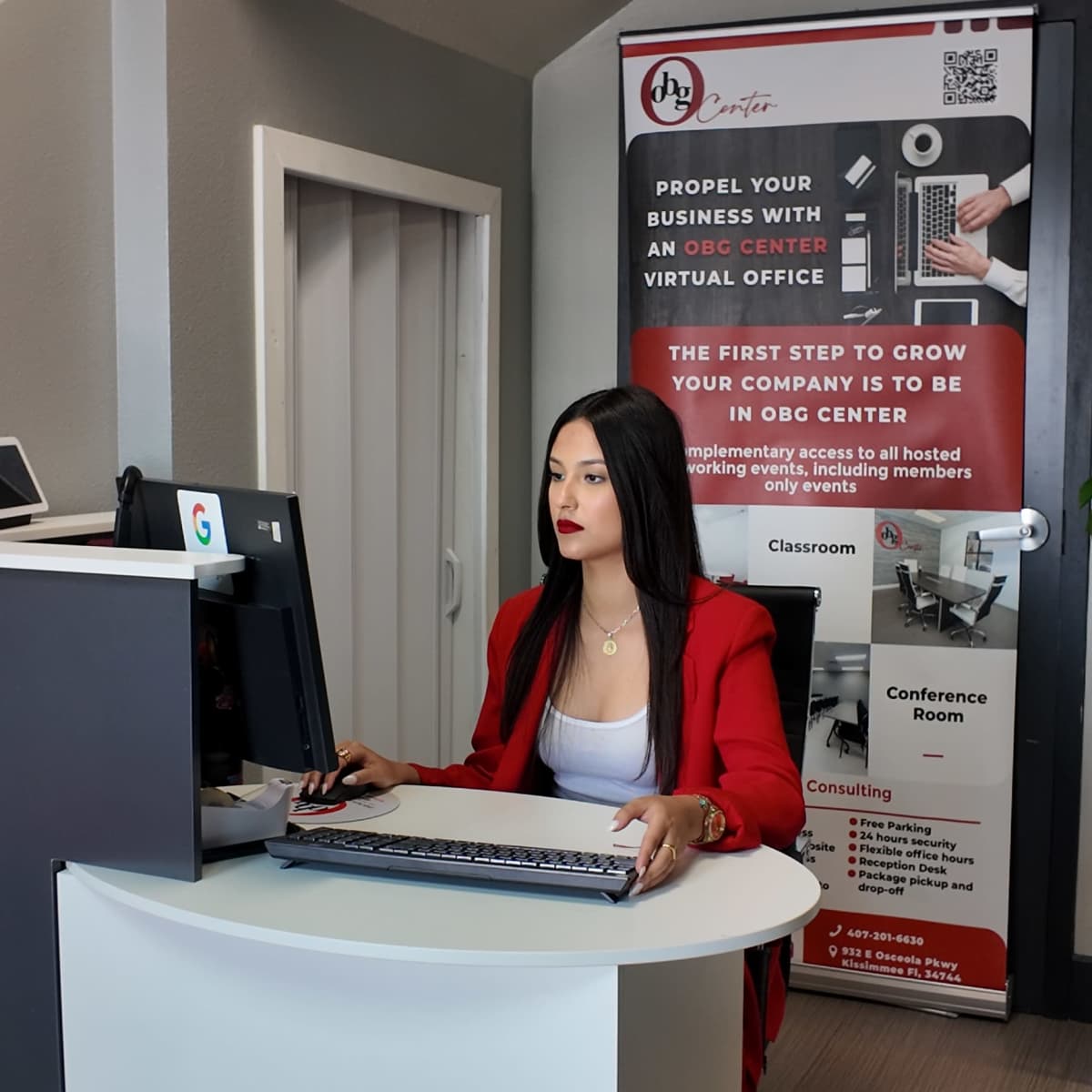 A woman in a red blazer works at a desk in an office space featuring a promotional banner for a virtual office service.