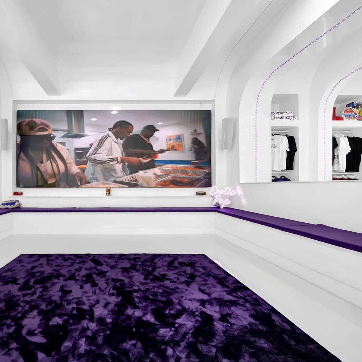 A modern, minimalist interior featuring white walls and a large screen displaying people preparing food, complemented by purple seating and a plush rug.
