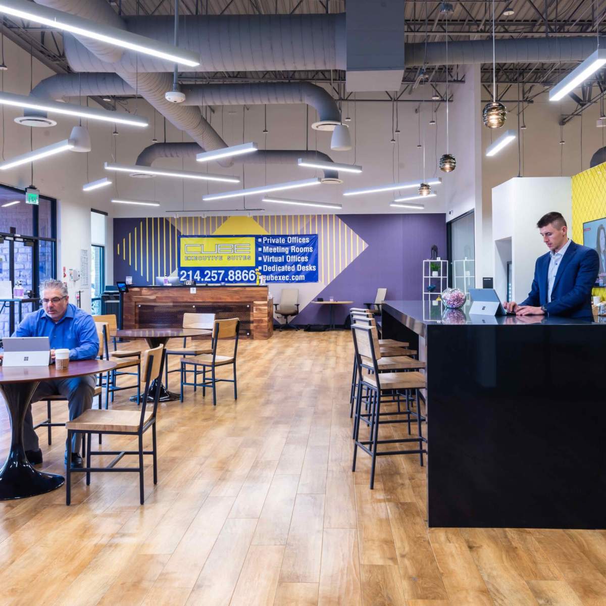 A modern office space with a reception area, seating arrangements, and a man working on a laptop at a counter.