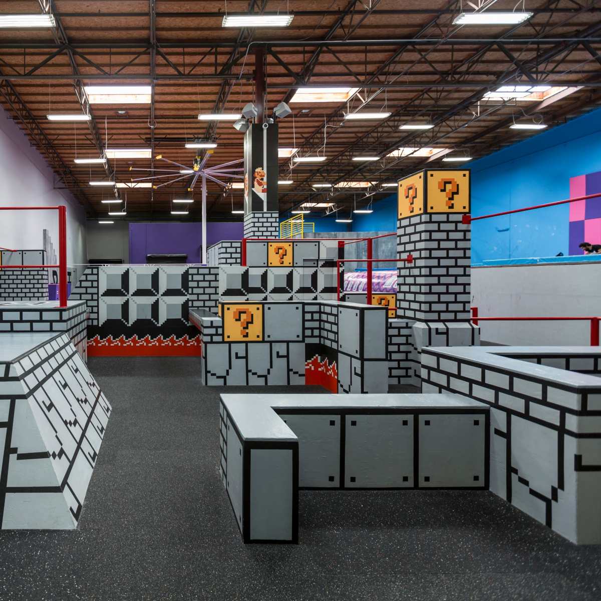 An indoor play area designed to resemble a video game world, featuring obstacles like blocky structures, ramps, and a grid pattern on the floor.