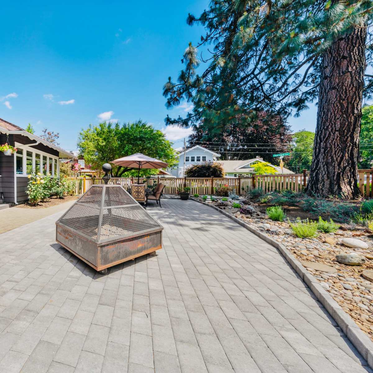 A stone house with a bright red door is surrounded by a paved patio and landscaped garden, featuring a fire pit and outdoor seating area.