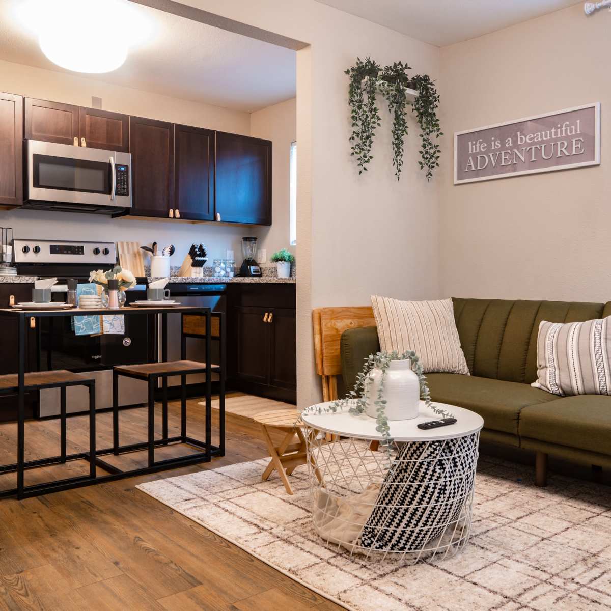 A modern living space featuring a kitchenette, a green couch, a coffee table, and a wall with a motivational sign.