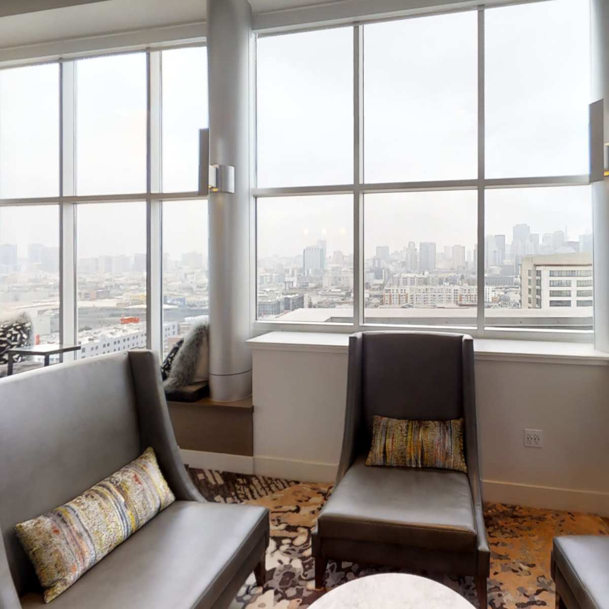 A modern lounge area with two gray chairs and a panoramic window displaying a city skyline.
