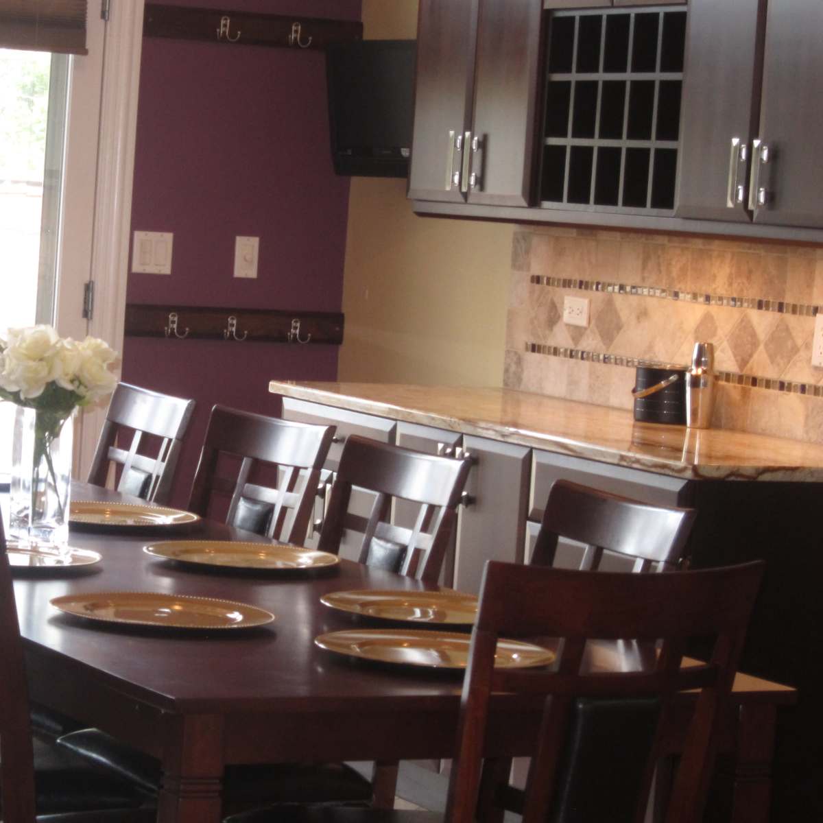 A dining table set for a meal is arranged in a modern kitchen with a vase of white flowers and empty plates.