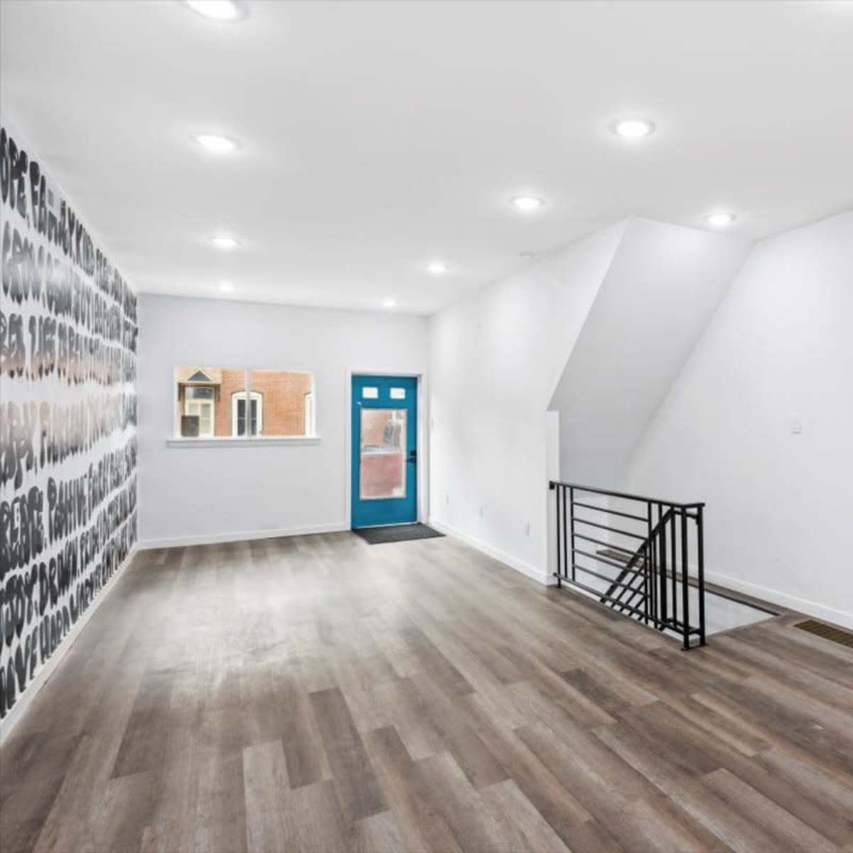 A spacious, modern interior of a room featuring a large window, a set of stairs, and a flat-screen TV mounted on the wall.