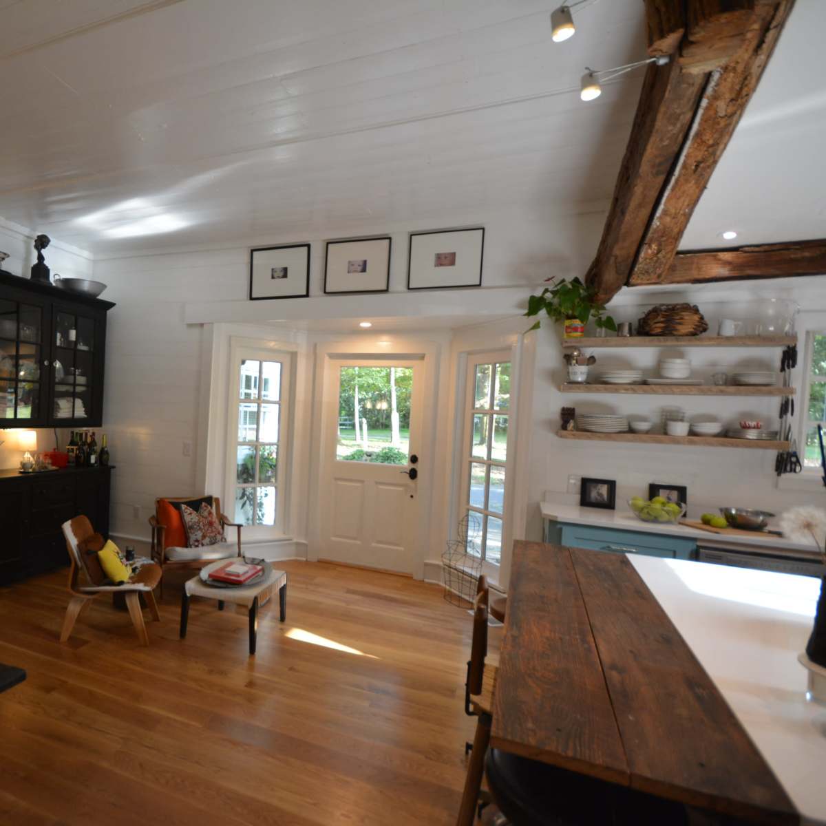 A bright, open kitchen and dining area with wooden floors, a large window, and a door leading to an outdoor space.