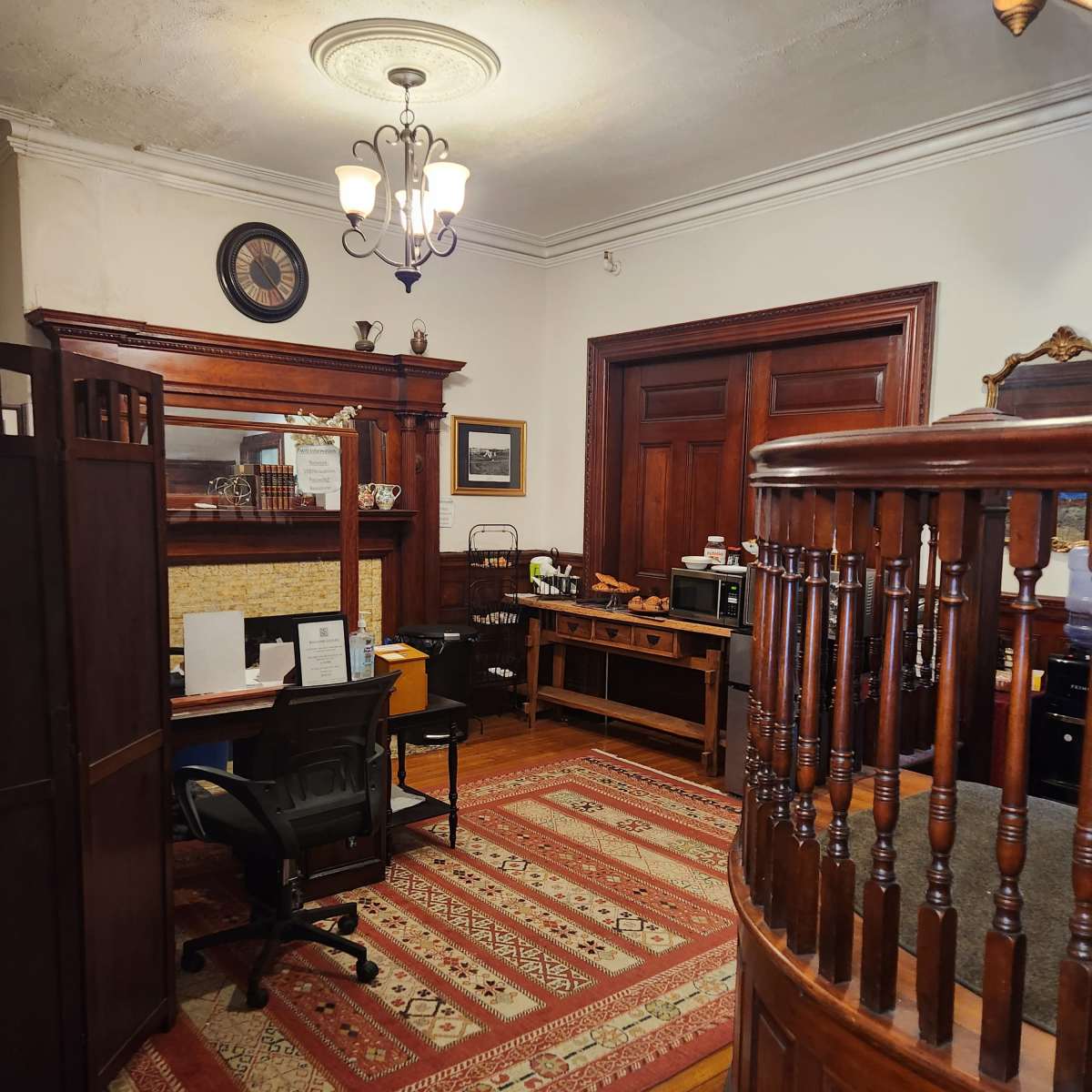 A well-furnished office with a large wooden reception desk, a black office chair, and ornate decor, including a chandelier and a patterned rug.