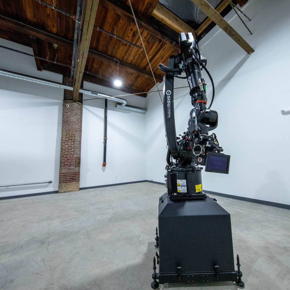 A robotic arm is positioned in the center of a spacious room with high ceilings and a concrete floor.
