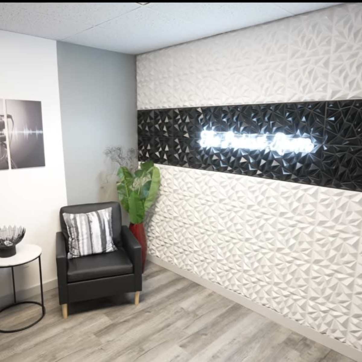 A modern interior space featuring two black chairs, a small round table with a decorative bowl, and a textured wall with illuminated text.