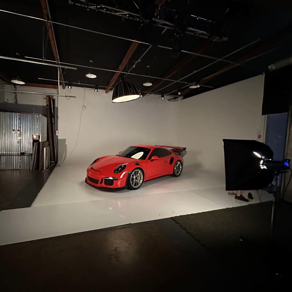 A bright red sports car is displayed on a white backdrop in a photography studio, surrounded by professional lighting equipment.