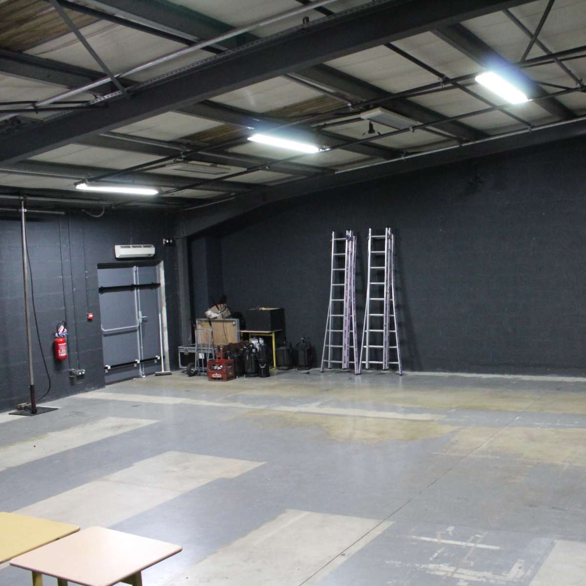 An empty warehouse space features a concrete floor, gray walls, and two ladders against the back wall.