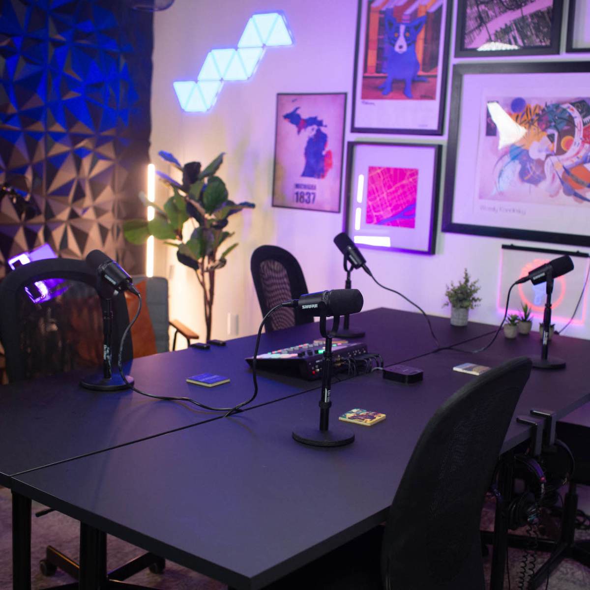 A modern podcast studio with a large black table, several microphones, and colorful wall decorations.