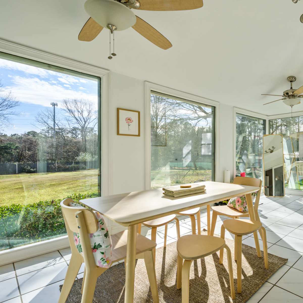 A bright sunroom features large windows, a table with four chairs, and a door leading to an outdoor area.