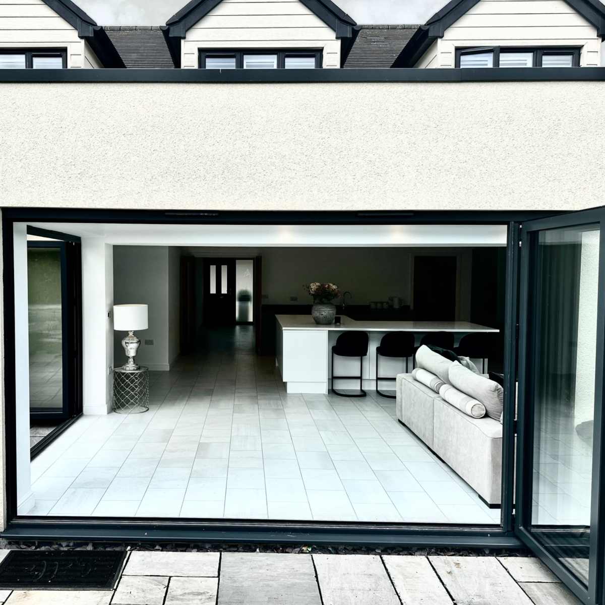 A modern home with large glass doors that open to a spacious interior featuring a kitchen island and a living area.