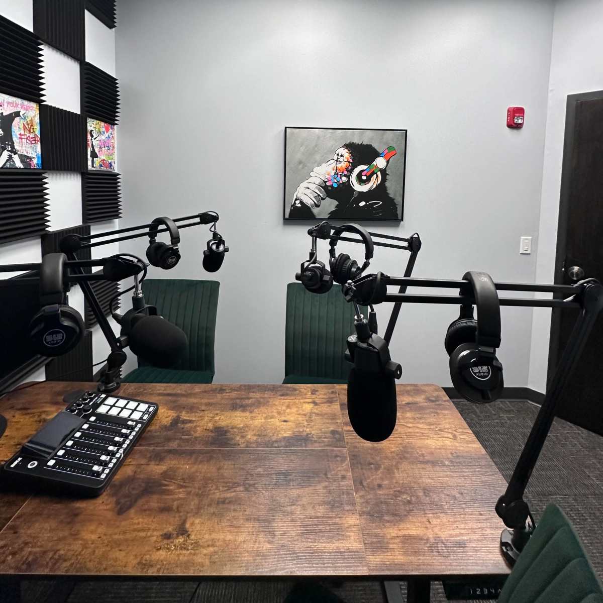 A recording studio features a wooden table with microphones and headphones set up, alongside colorful artwork on the walls.