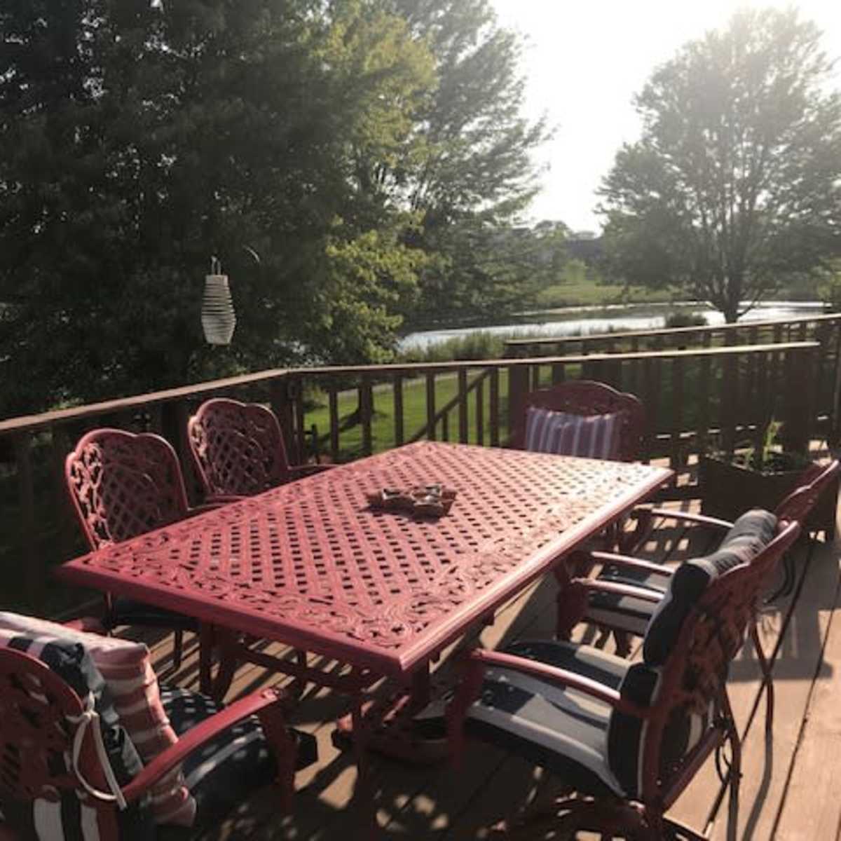 A red metal table and chairs are set on a wooden deck overlooking a pond and trees.