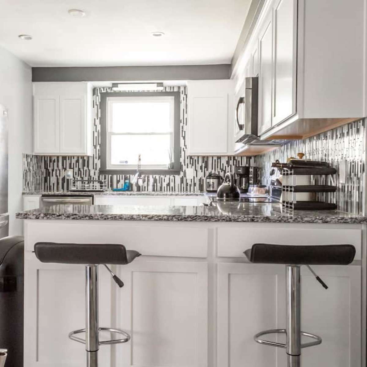 A modern kitchen features white cabinetry, a granite countertop, stainless steel appliances, and a tiled backsplash.
