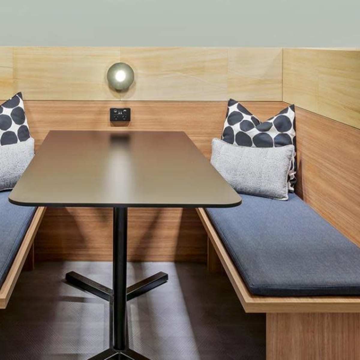A small booth with wooden partitions, featuring a table and two benches with cushions on each side.