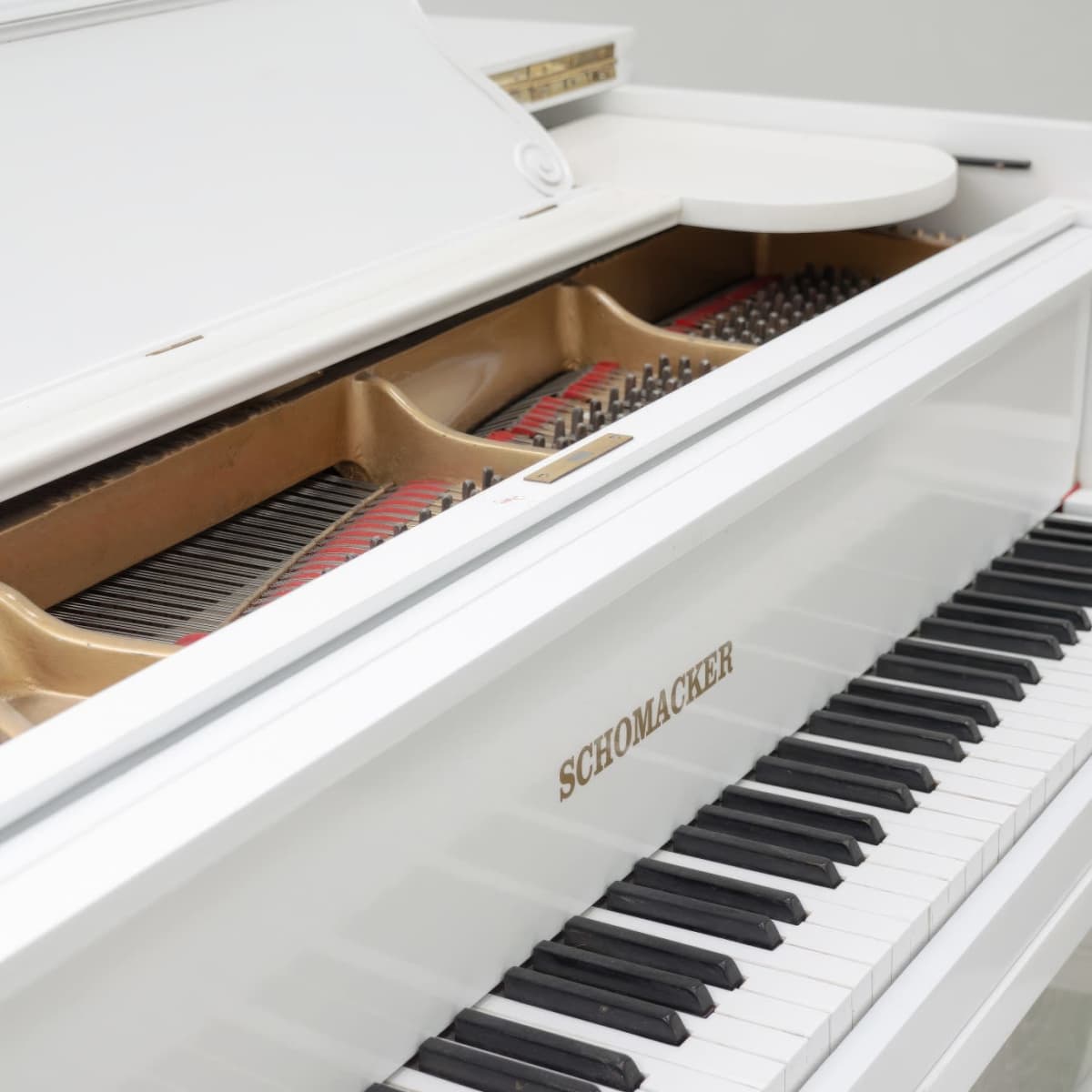 A white piano with the brand name "Schoenacker" visible on its front, featuring a polished surface and open lid that reveals the strings inside.