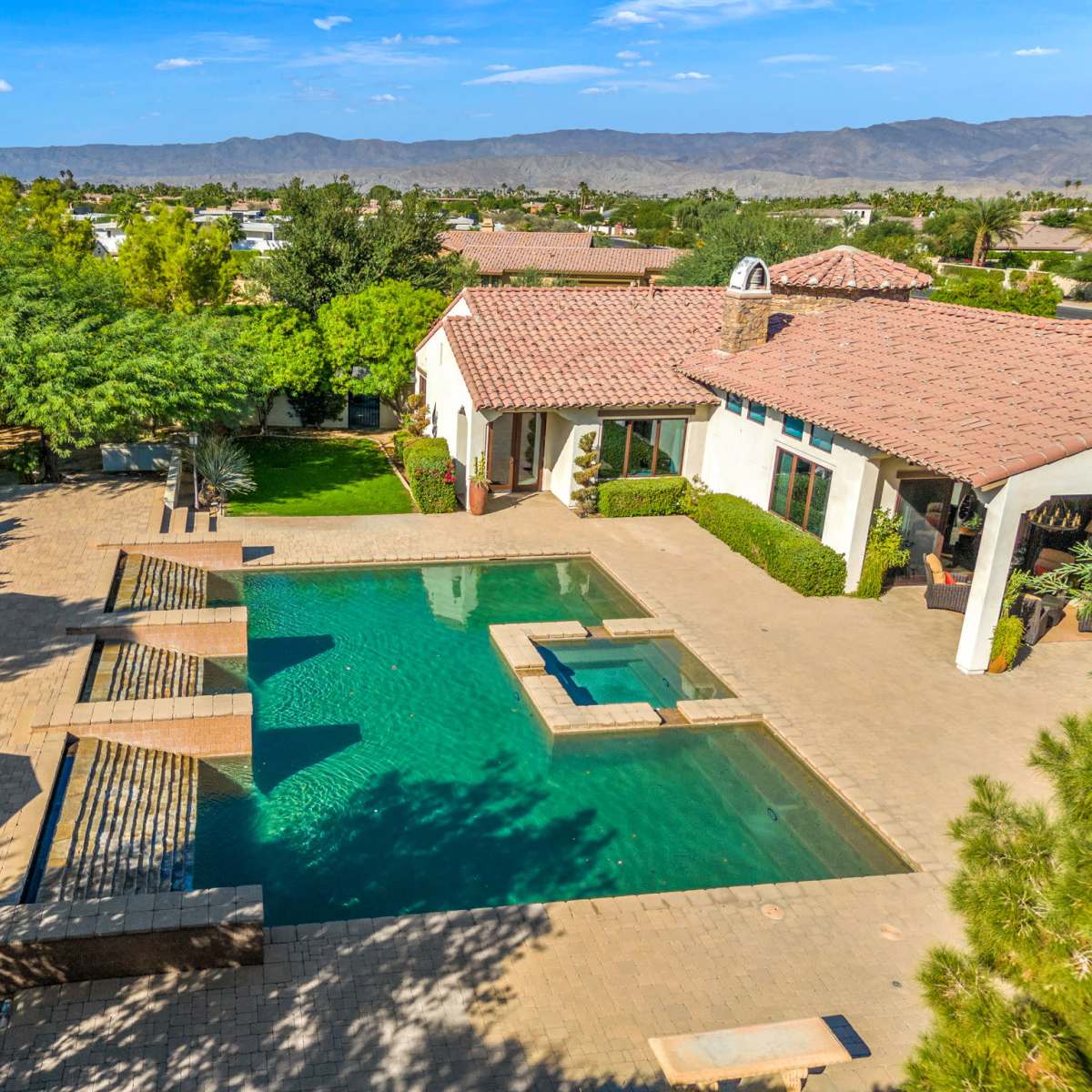A residential backyard with a swimming pool, surrounded by landscaped greenery and a patio area with lounge chairs.