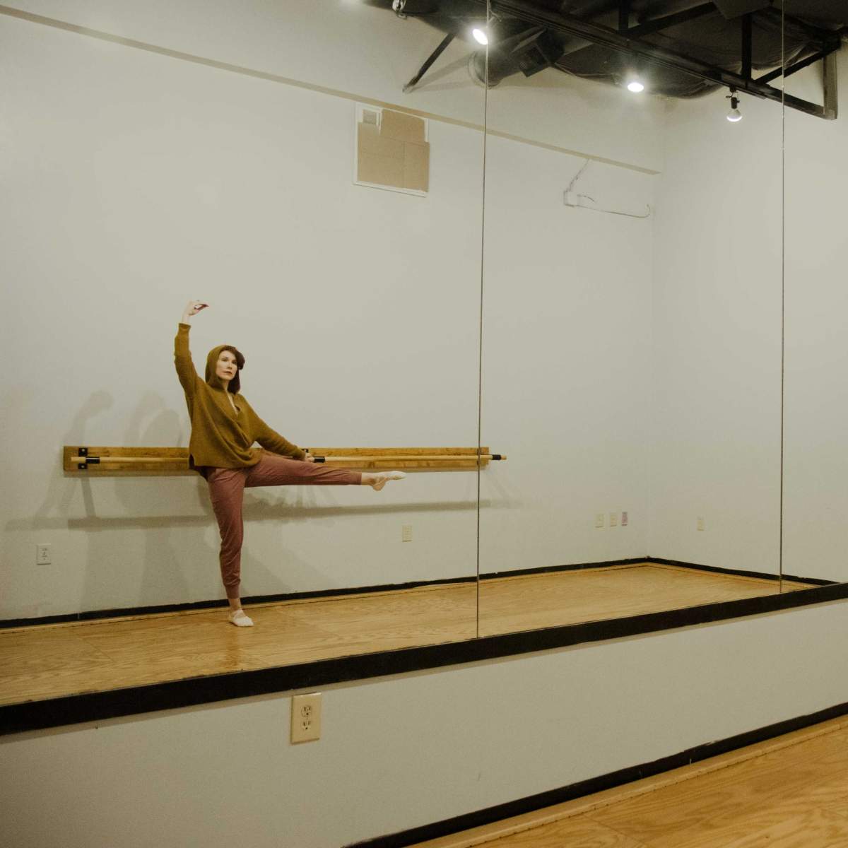 A person is performing a dance move in a studio with wooden floors and mirrored walls.