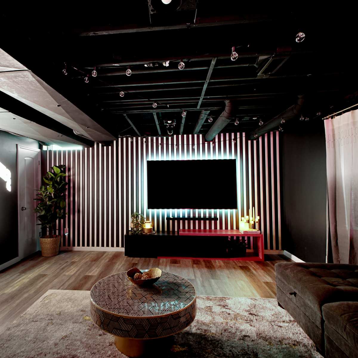 The interior of a modern living room features a large wall-mounted TV, decorative lighting, and a plush couch with a round coffee table in the center.