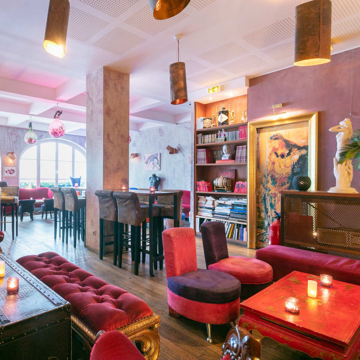 A colorful bar interior with vintage seating, a variety of plants, and dim lighting, creating a cozy atmosphere.