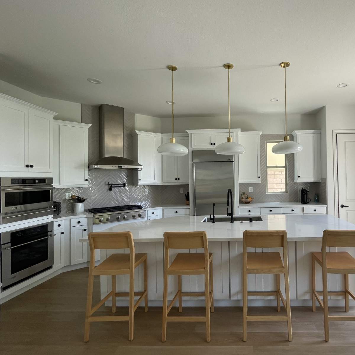 A modern kitchen features white cabinetry, stainless steel appliances, and a large island with four wooden bar stools.