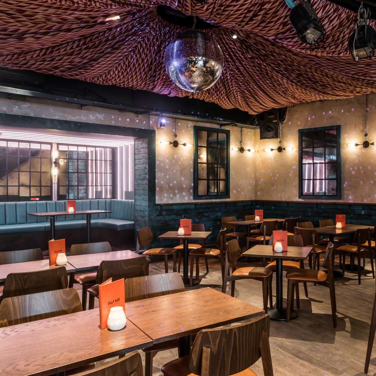 An interior of a restaurant with wooden tables and chairs, featuring a disco ball hanging from the ceiling and illuminated by soft lighting.