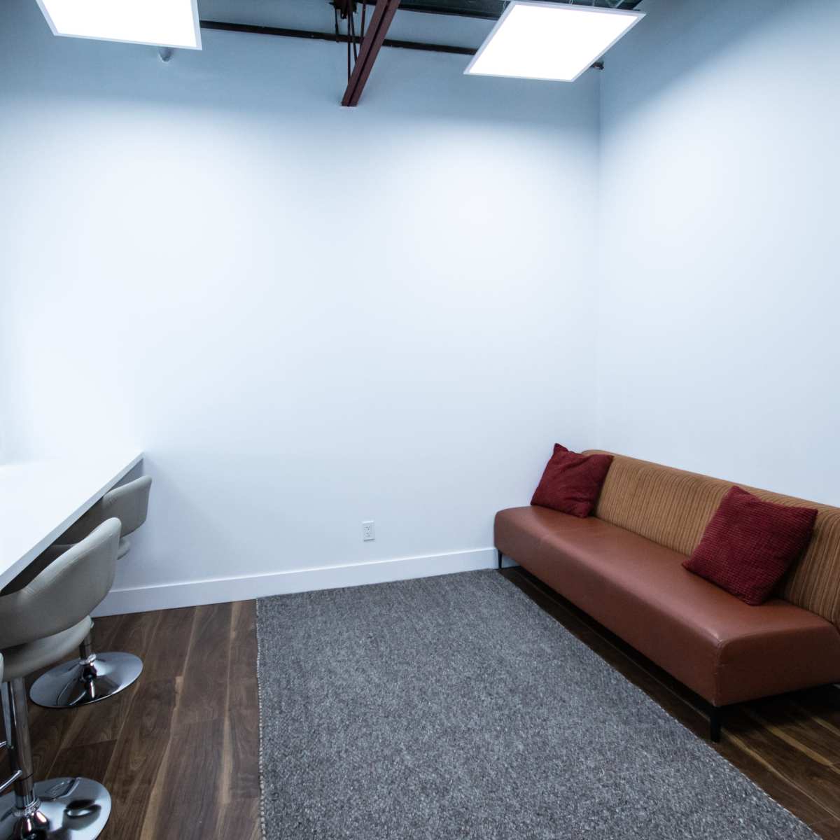 A small room with a brown couch, a long white table with two mirrors, and four modern stools on a wooden floor.