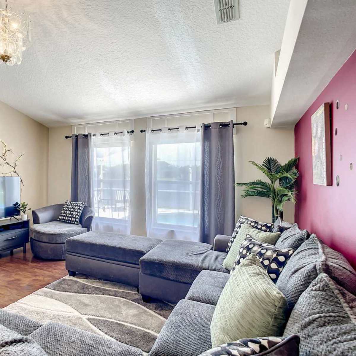 A modern living room features a sectional sofa, a television, and large windows with curtains.
