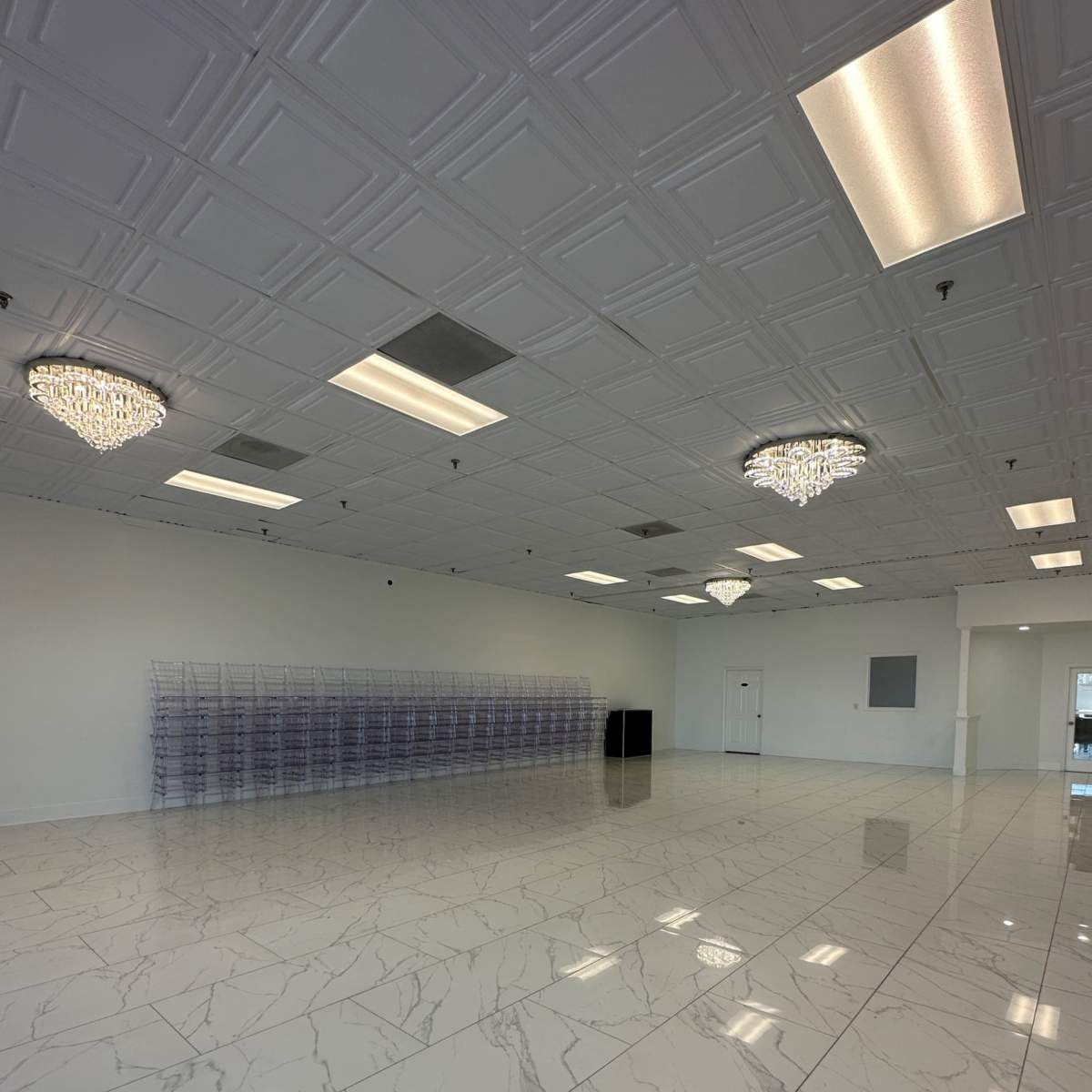 A large, empty commercial space with white marble flooring, ceiling lights, and two crystal chandeliers.