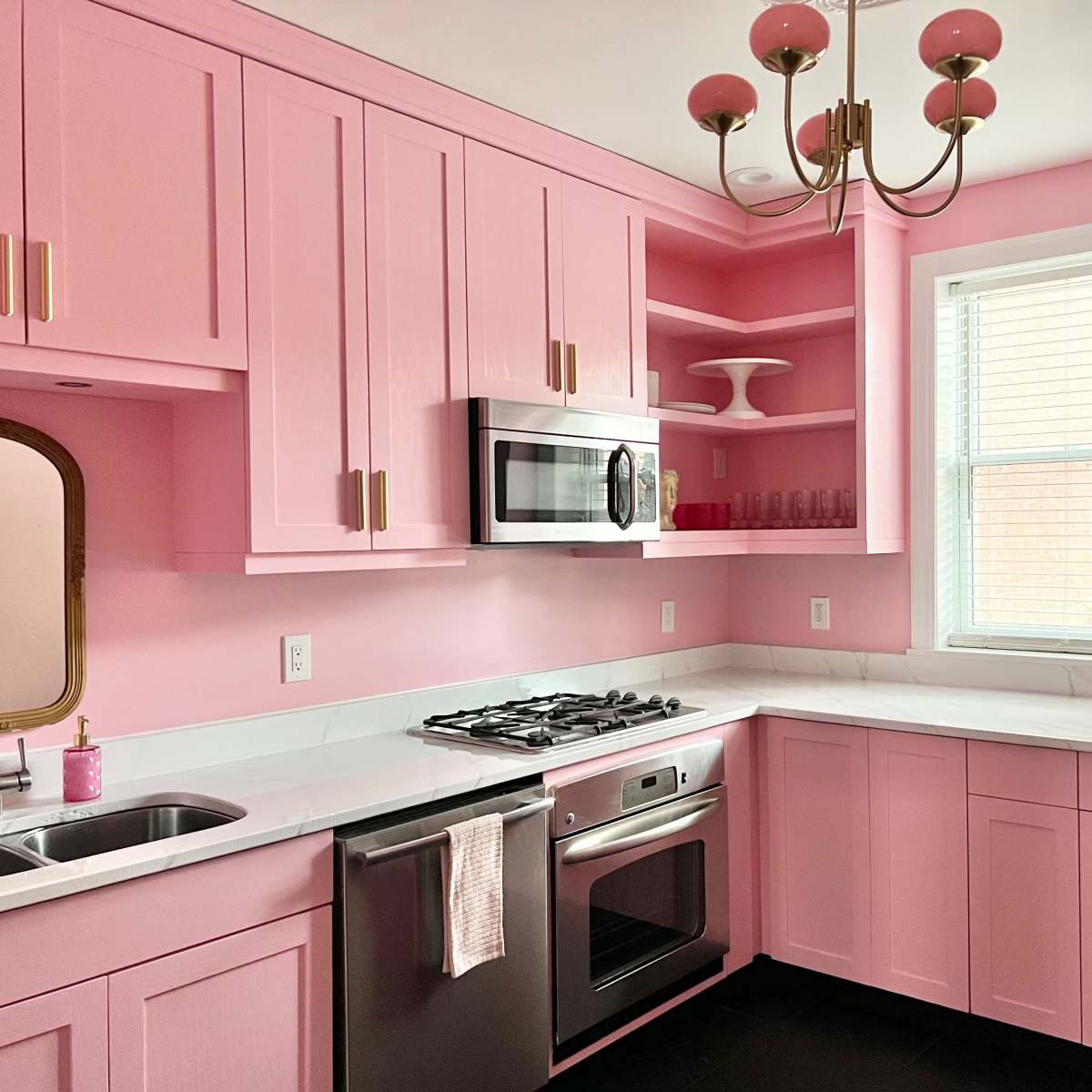 A kitchen with pink cabinets, a silver microwave, and a window illuminating the space.