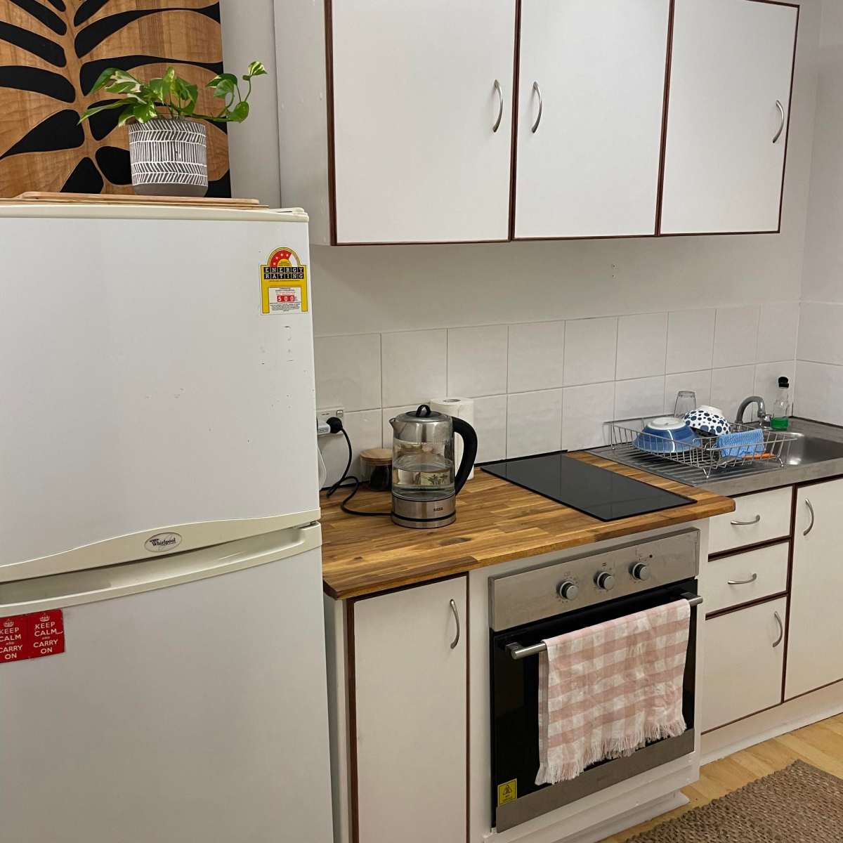 A kitchen with white cabinets, a wooden countertop, a refrigerator, a kettle, and a stove.