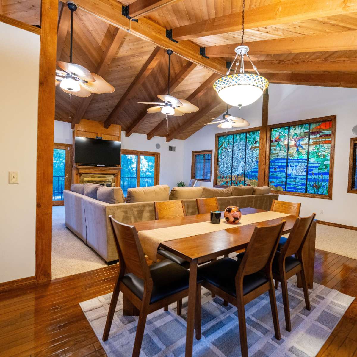 A dining area with a wooden table and chairs, adjacent to a spacious living room featuring a sectional sofa and large windows with a view of the outdoors.